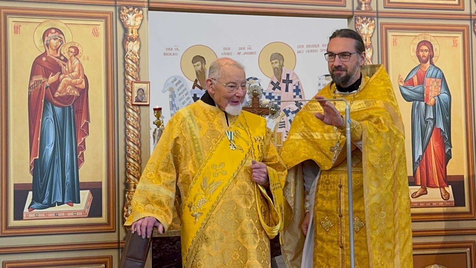 Pfarrer Alexej Veselov (r.) überreicht Diakon Elmar Kalthoff anlässlich seines 90. Geburtstags den Orden des ehrwürdigen Seraphim von Sarow, der ihm von Patriarch Kyrill von Moskau und der ganzen Rus verliehen wurde. Foto: Gemeinde